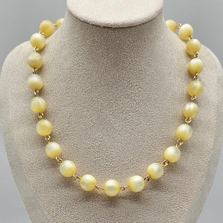Cream colored moonglow beaded necklace on a mannequin bust with a gray background