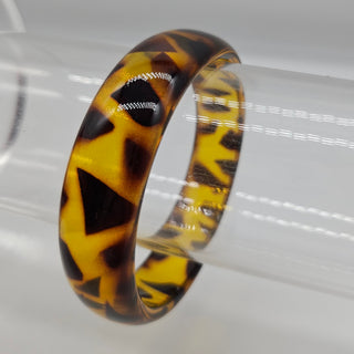 A glossy tortoiseshell-patterned resin bangle displayed on a clear cylindrical stand against a light gray background.