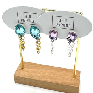 Pair of earrings with blue and purple gemstones on a display stand with 'Leetie Lovendale' branding.