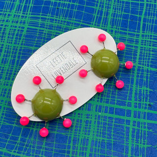 OlIve green earrings with hot pink beads radiating from center with posts on a blue and green plaid background.