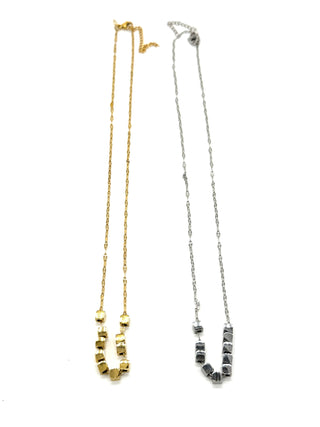 A pair of necklaces, in silver and gold, on a white background. Each is a fine chain with several cube beads at the center.
