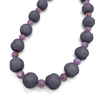 Closeup of necklace featuring dark gray and lilac lucite beads laid on a white background.