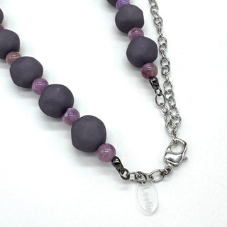 Closeup of adjustable necklace featuring dark gray and lilac lucite beads laid on a white background.