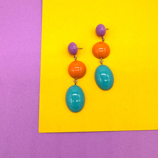 Colorful earrings with purple, orange, and blue beads on a yellow and purple background
