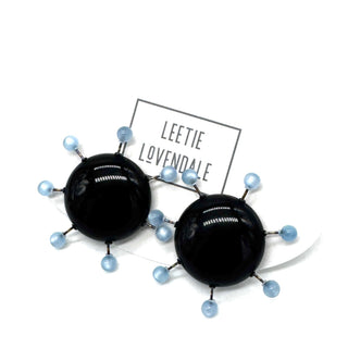 Black circular earrings with blue beads on a white background, featuring the brand 'Leetie Lovendale'.