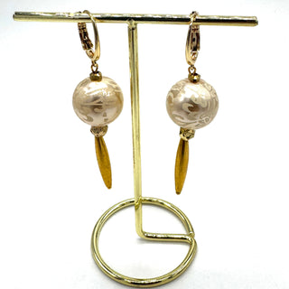 Dangle earrings with floral cream colored beads and golden accents hanging from a stand on a white background.