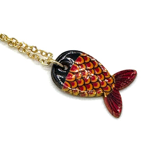 A gold chain necklace with a fish-shaped pendant featuring red, orange, and yellow scales on a black background, shown against a plain white background.