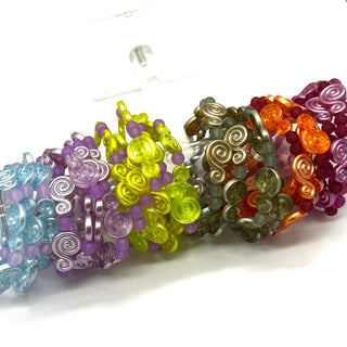 A set of colorful beaded bracelets with spiral and round bead designs, shown in multiple colors including purple, yellow, gray, orange, and blue on a white background.