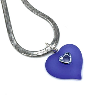 A silver snake chain necklace with a periwinkle heart-shaped pendant featuring a small metallic heart in the center, shown on a plain white background.