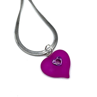 A silver snake chain necklace featuring a hot pink heart-shaped pendant with a smaller metallic heart cutout in the center, shown on a plain white background.