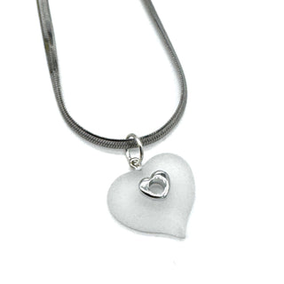 A silver snake chain necklace featuring a frosted white heart-shaped pendant with a small, polished silver heart inset in the center, shown against a plain white background.