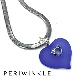 A silver snake chain necklace with a purple heart-shaped pendant featuring a small silver heart cutout in the center, shown on a white background with the brand name PERIWINKLE at the bottom.