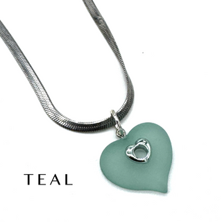 A teal heart-shaped pendant necklace with a silver snake chain and a small silver heart detail, shown on a white background with the word 'TEAL' printed in the lower left.