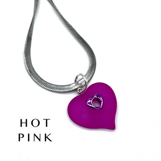 A silver snake chain necklace with a hot pink heart-shaped pendant featuring a smaller silver heart cutout in the center, shown on a white background with the text 'HOT PINK' in the lower left.