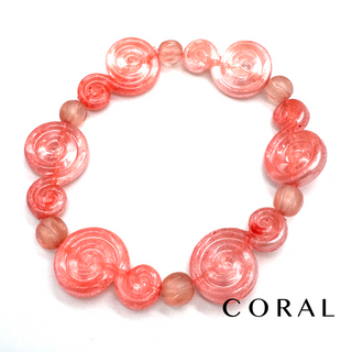 A coral pink beaded bracelet featuring large spiral-shaped beads and smaller round beads, displayed on a clean white background with the word 'CORAL' printed in black at the bottom right.