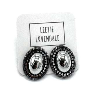 A pair of oval stud earrings with shiny silver-toned centers and dark textured outer borders, displayed on a white branded backing card that reads LEETIE LOVENDALE.