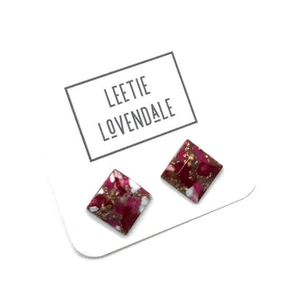 A pair of square stud earrings with a deep magenta-pink and white marbled pattern and embedded gold flakes, displayed on a white card printed with the brand name 'LEETIE LOVENDALE'.
