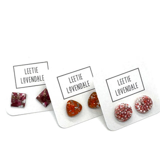 Three pairs of handmade stud earrings displayed on white backing cards with the brand name 'LEETIE LOVENDALE' printed on them. The earrings are made from glass.