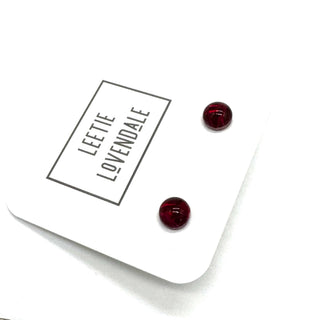 A pair of small round stud earrings in deep red resin, displayed on a white branded card that reads 'LEETIE LOVENDALE'.