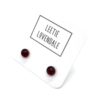 A pair of small round dark red stud earrings displayed on a white backing card with the brand name 'LEETIE LOVENDALE' printed in black text.