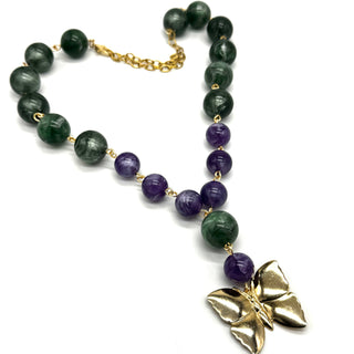 A beaded necklace featuring dark green and purple lucite beads connected by a gold-tone chain, with a textured gold butterfly pendant at the end, displayed on a clean white background.
