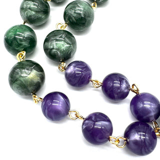 A beaded necklace featuring green and purple lucite beads separated by small gold chain links, shown on a clean white background.