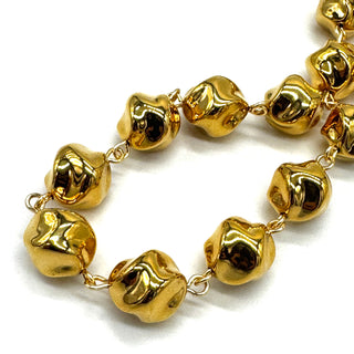 A close-up of a gold-toned beaded necklace with irregular, organic-shaped beads connected by small links, photographed on a plain white background.