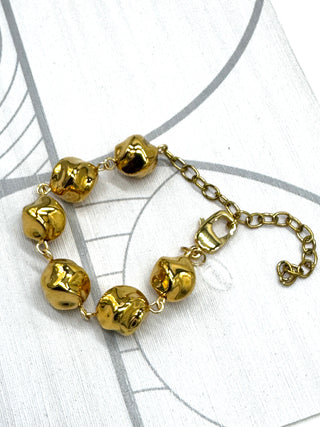 A gold-toned beaded bracelet with six irregular, polished beads connected by a delicate chain and extender clasp, displayed on a white background with faint gray circular line patterns.