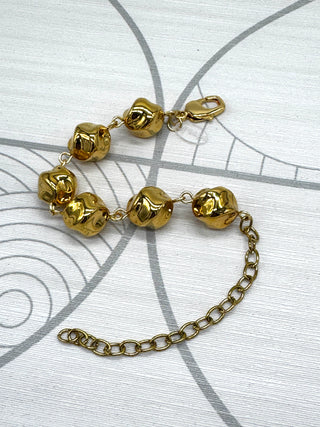 A gold-toned bracelet featuring textured, rounded beads connected by a delicate chain, with an adjustable lobster clasp and extender chain, displayed on a light gray patterned surface.