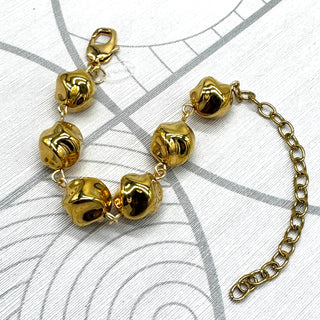 A gold-tone metal bracelet featuring textured, polished twisted round-shaped beads connected by small links, with a lobster clasp on one end and an adjustable extension chain on the other, displayed on a white patterned surface.